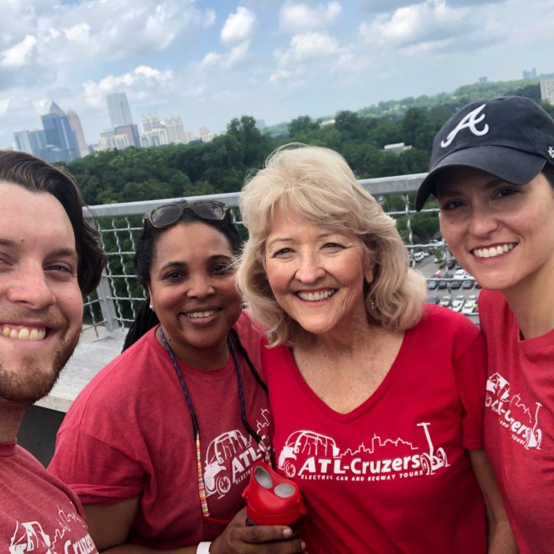 Four people in red shirts smiling on a rooftop with city skyline in the background.