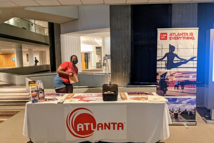 Indoor booth with Atlanta logo and a person standing beside brochures and a display banner.